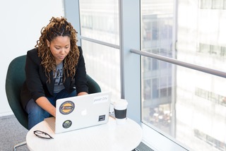 A woman seated at a table with her Macbook by a window