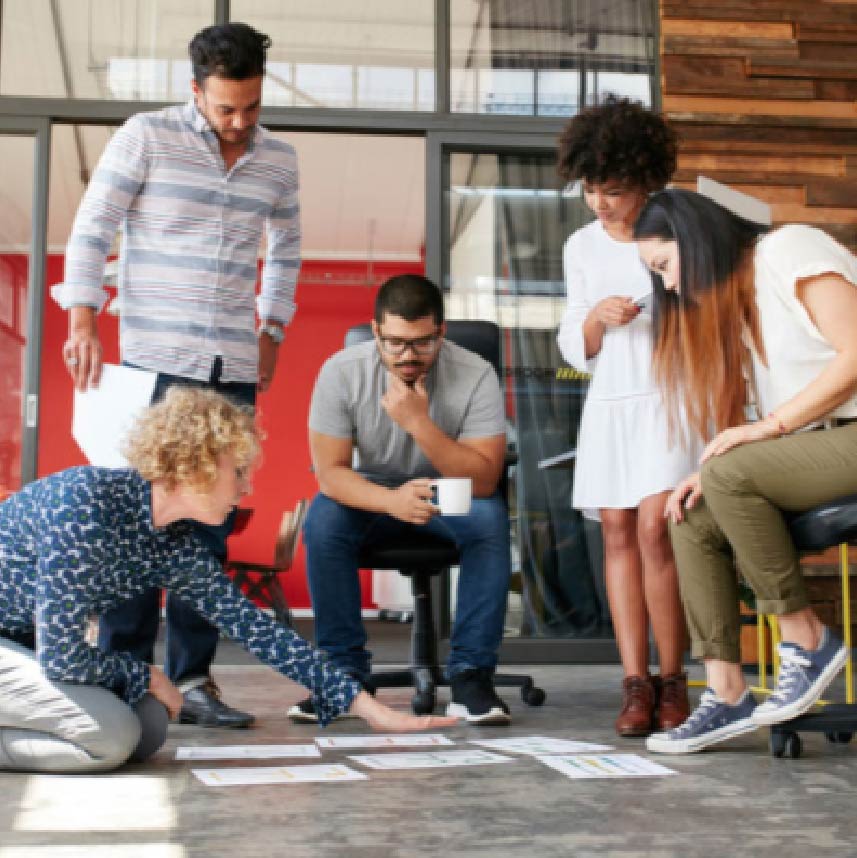 Several individuals studying several drawings laid out on the floor