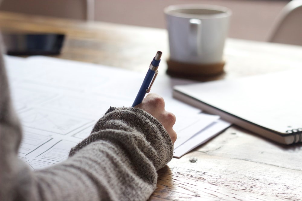 Person writing at a desk with a coffee mug in the background