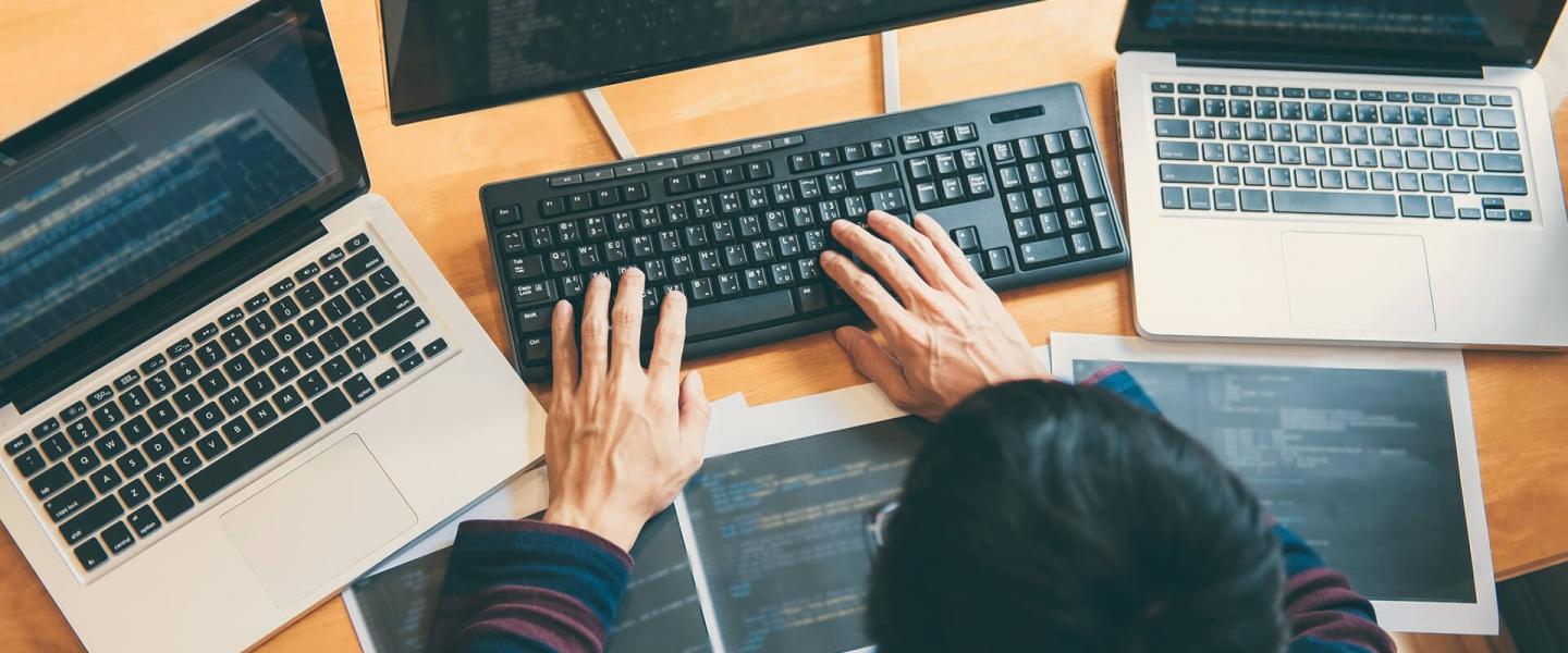 A man typing on a computer keyboard with a laptop on either side of the main computer