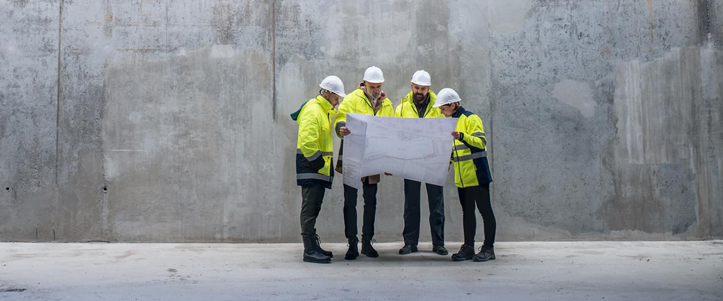 Four construction workers with hard hats looking at a plan