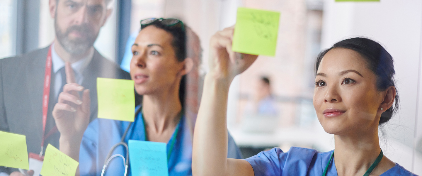 Three professionals looking at sticky notes on a glass panel