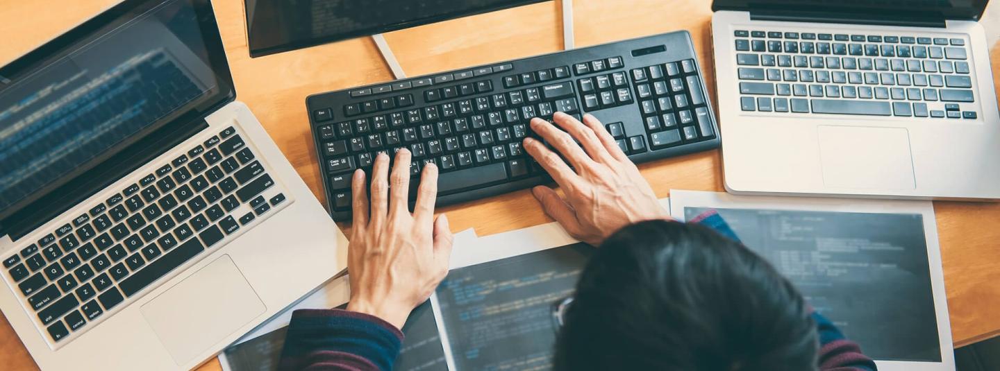 A man typing on a computer keyboard with a laptop on either side of the main computer