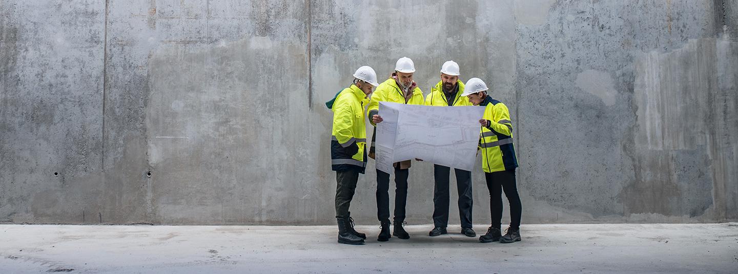 Four construction workers with hard hats looking at a plan