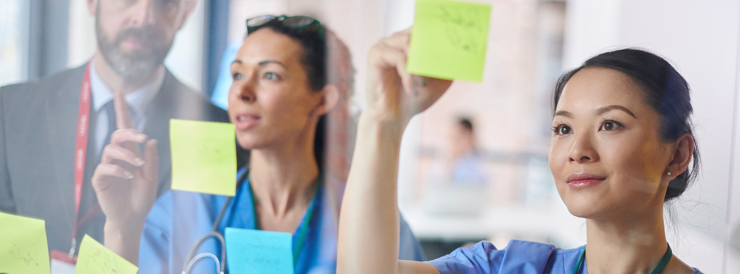 Three professionals looking at sticky notes on a glass panel