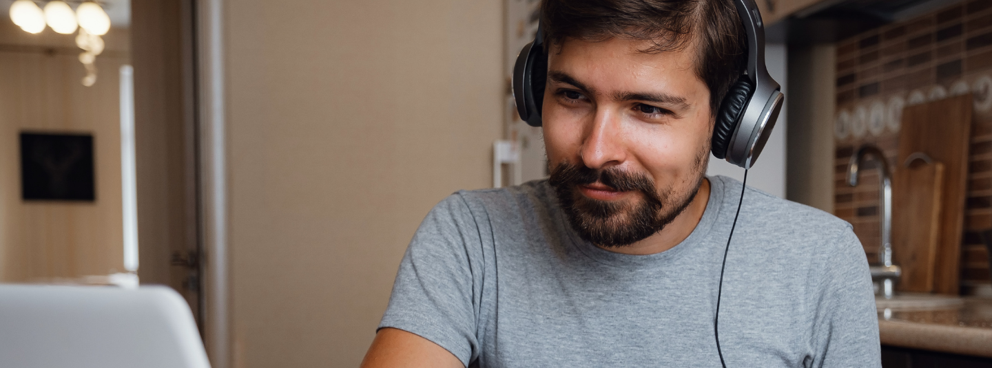 A smiling man wearing a headset looking at a computer monitor